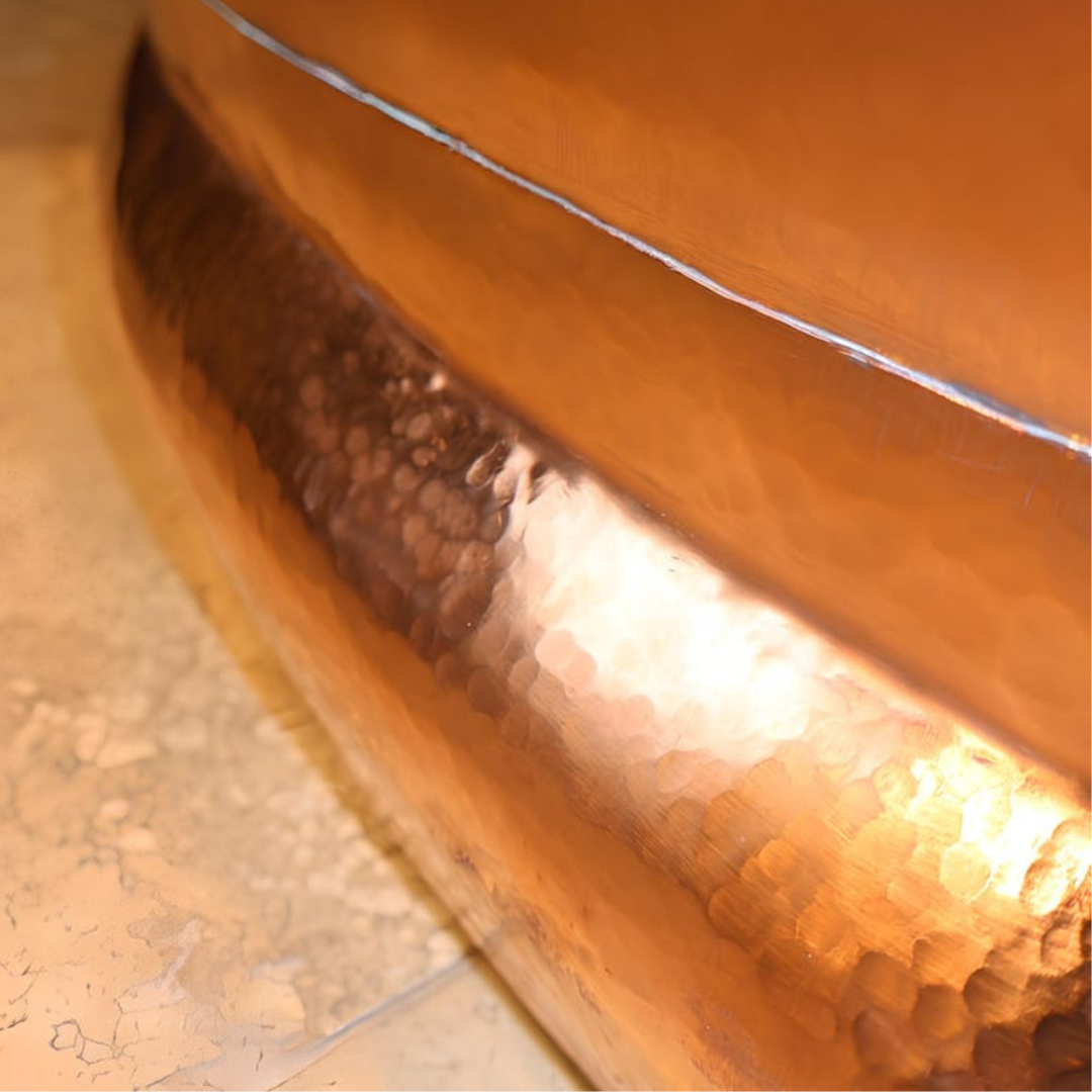 Hammered copper base curve — craftsmanship at the tub foot